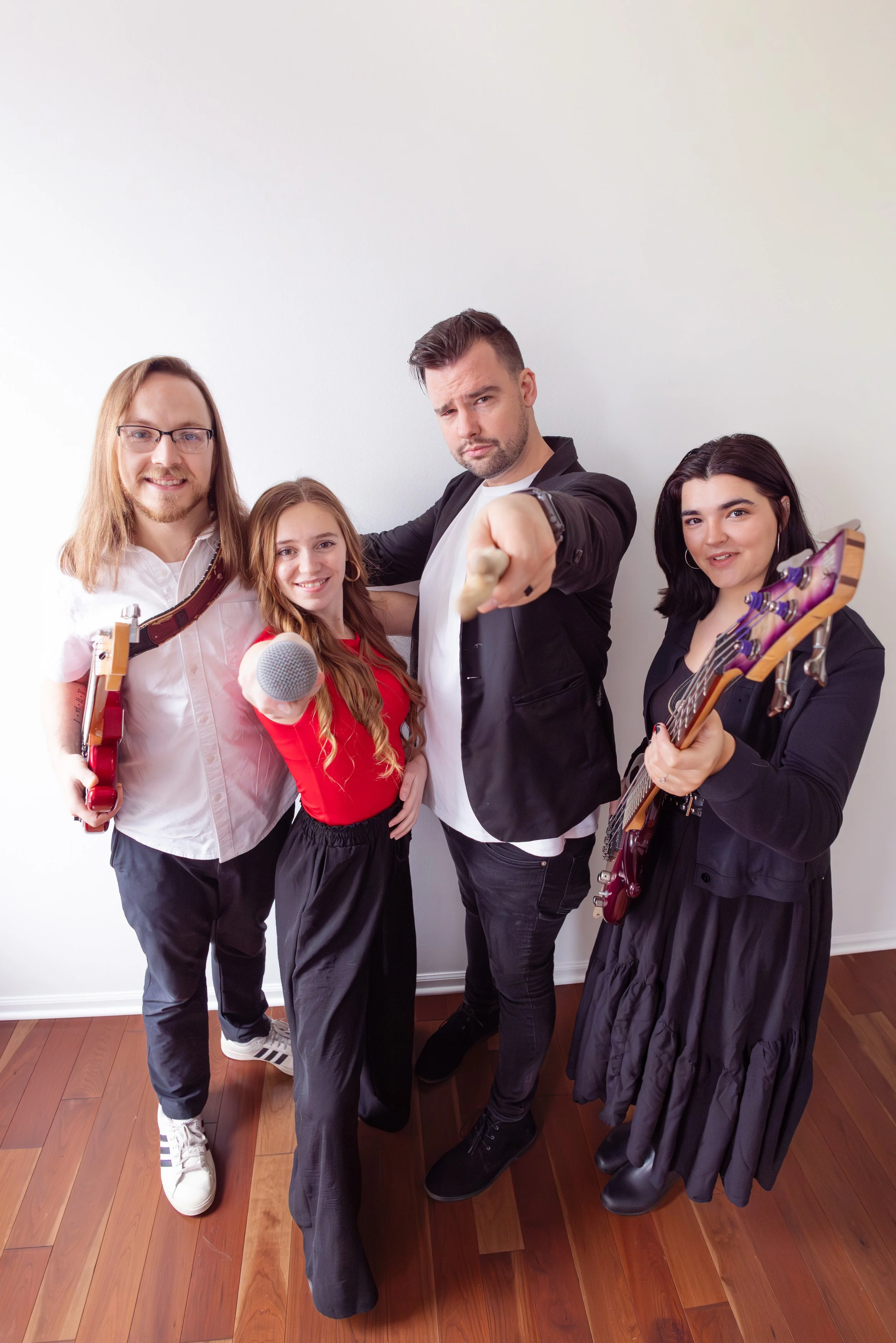 The Heartbeats Metro Detroit Wedding and Event Band holding musical instruments and posing confidently indoors, with a plain white wall as background.