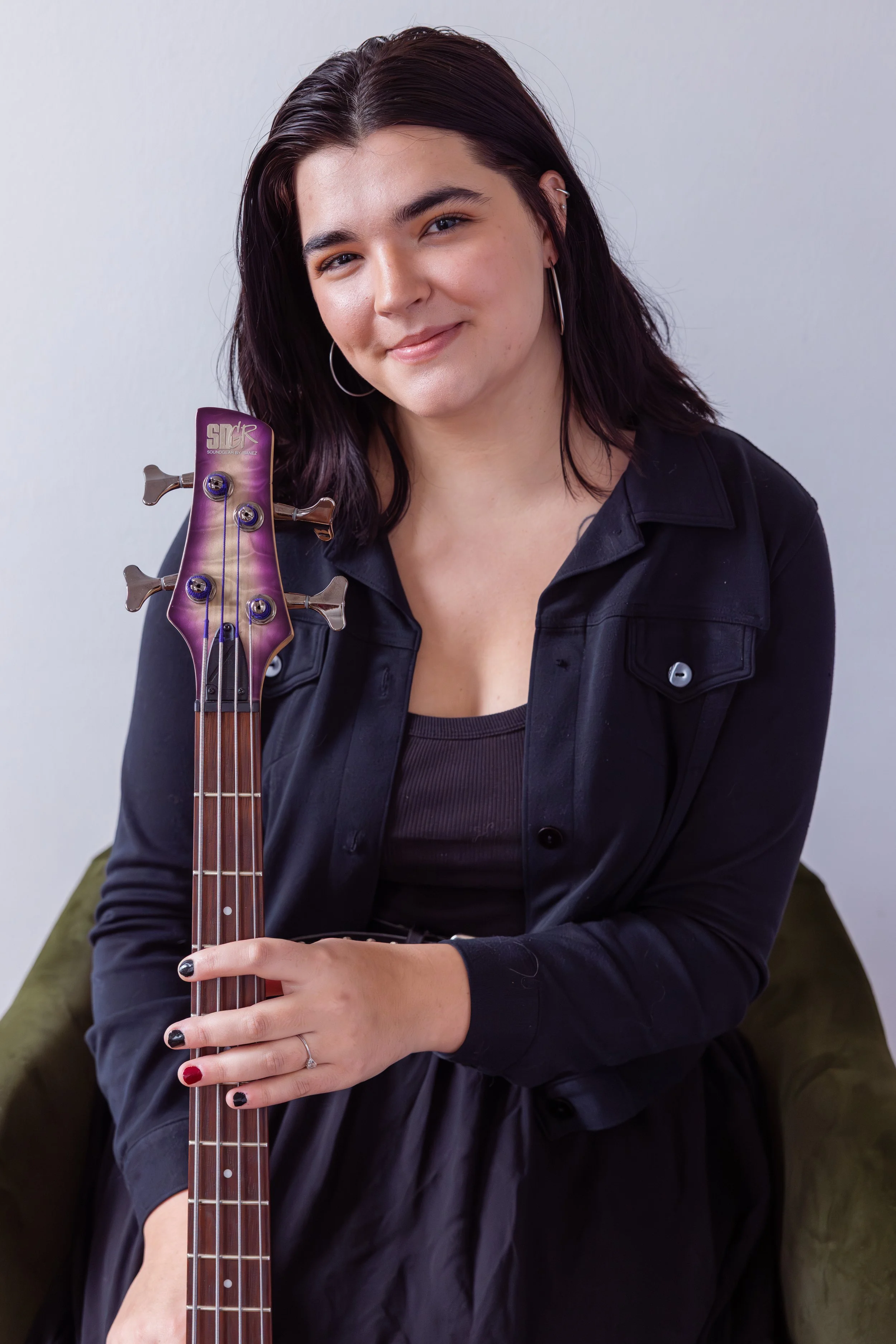 A young woman with dark hair and hoop earrings smiling while holding a guitar.
