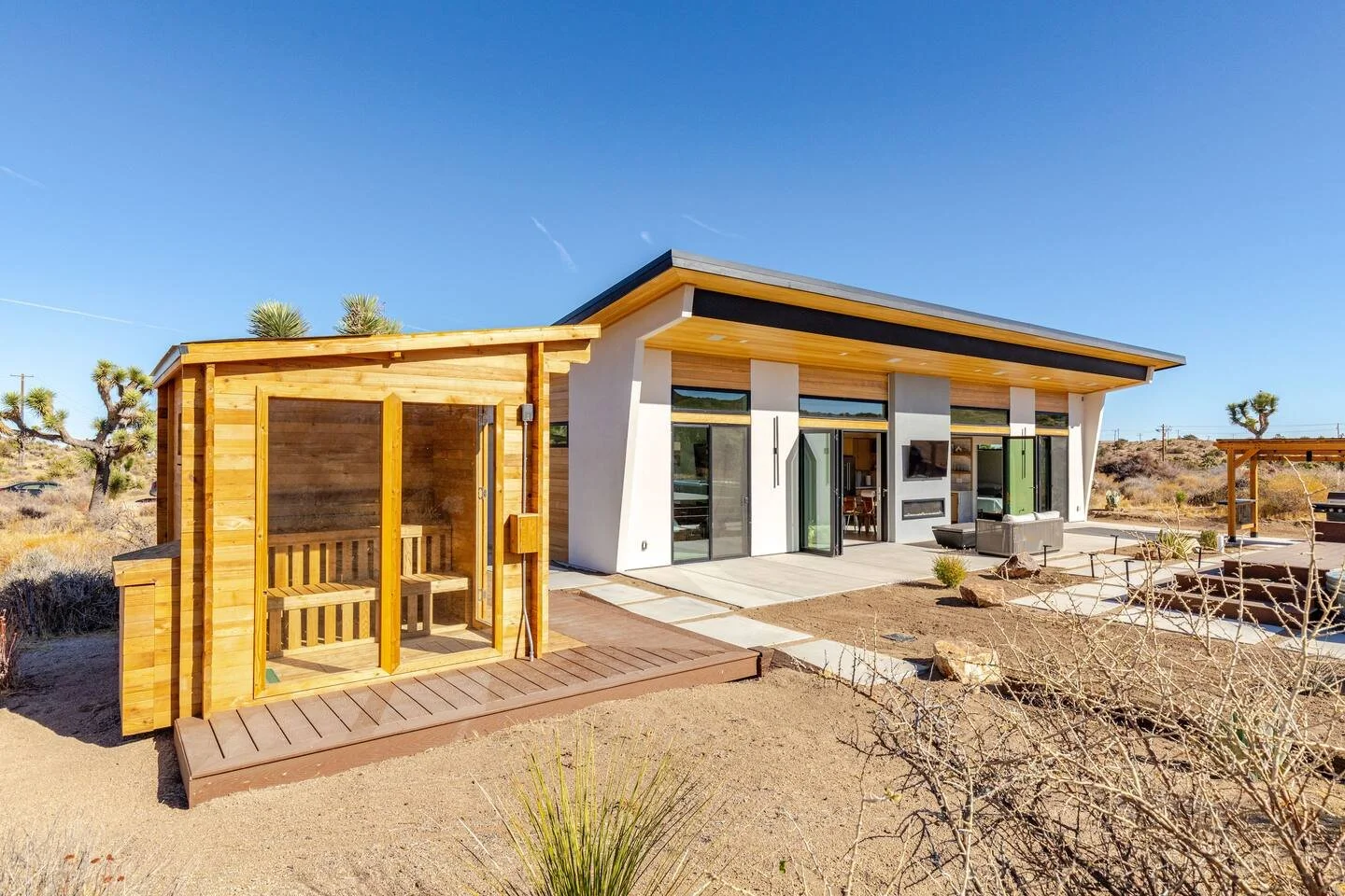 Modern house with large glass windows and a small wooden sauna in desert landscape