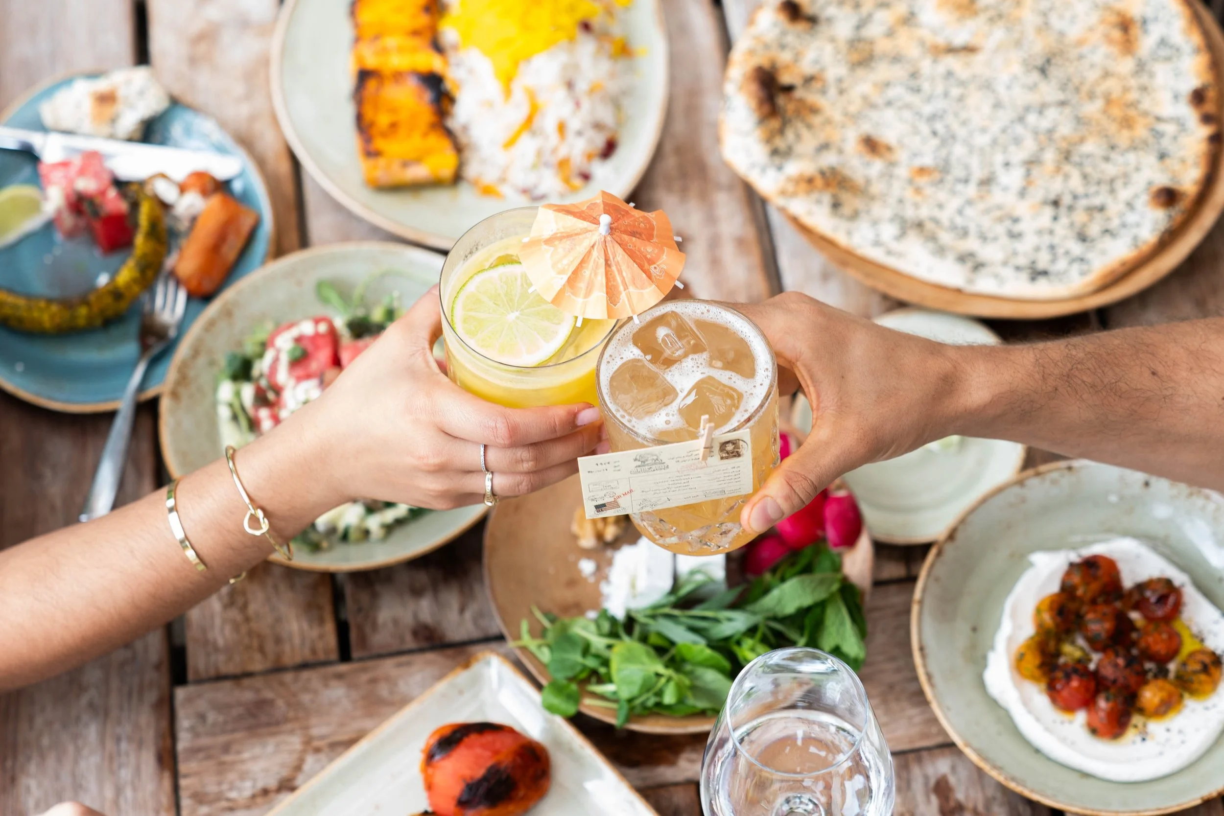 An image of farm table food with drinks toasting