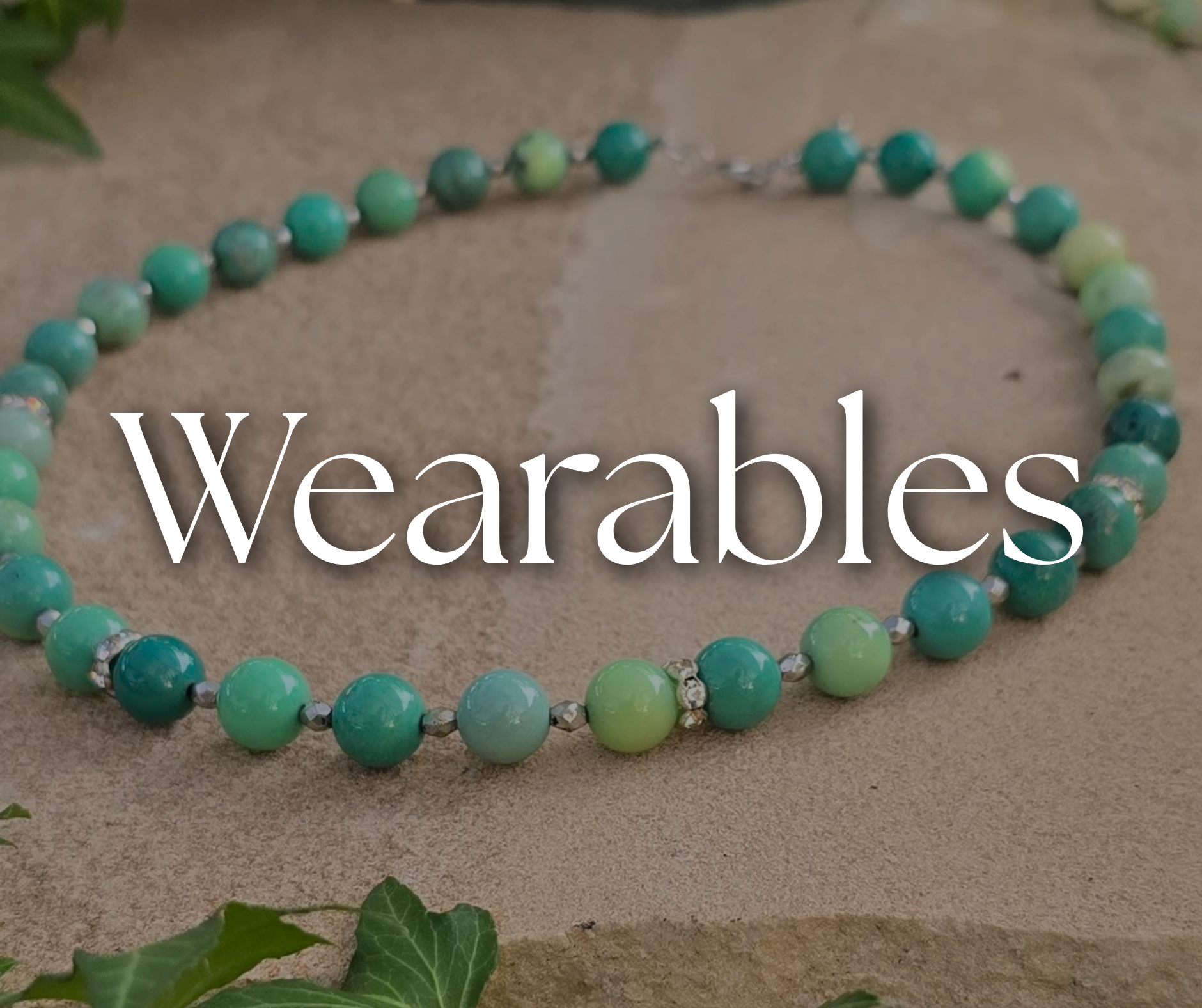 A necklace made of various shades of green beads arranged in a circle on a light stone surface, with the word 'Wearables' written across the center.