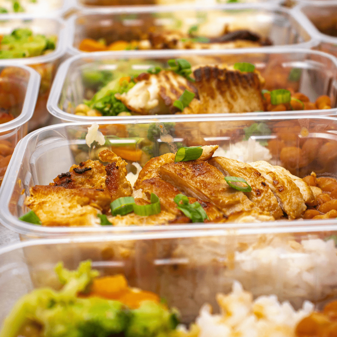Close-up of stacked meal-prep containers holding sliced roasted chicken breast over rice with mixed vegetables, topped with chopped green onions.