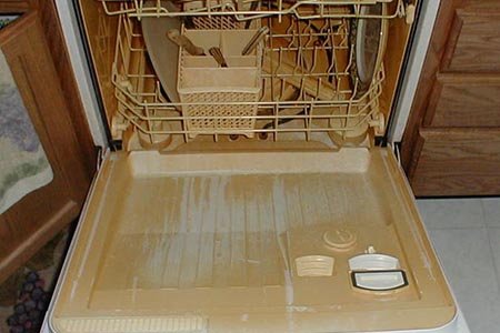 Stained dishwasher with discolored dishes drying inside.