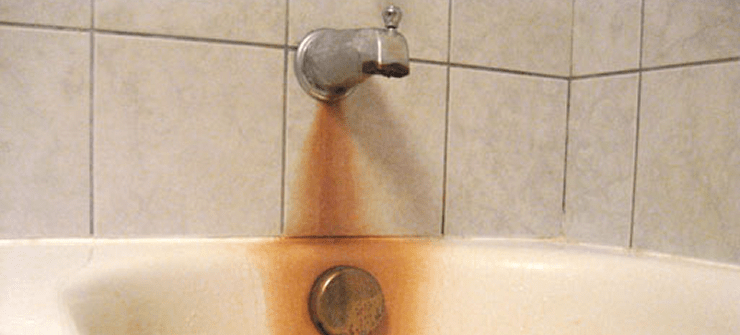 A bathroom sink with iron-colored stains and rust around the faucet and drain.