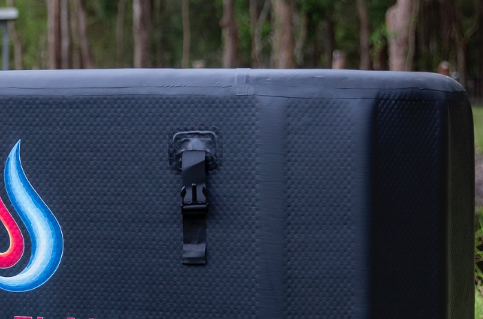 Close-up view of a black textured surface with a strap and clip, outdoors with trees in the background.