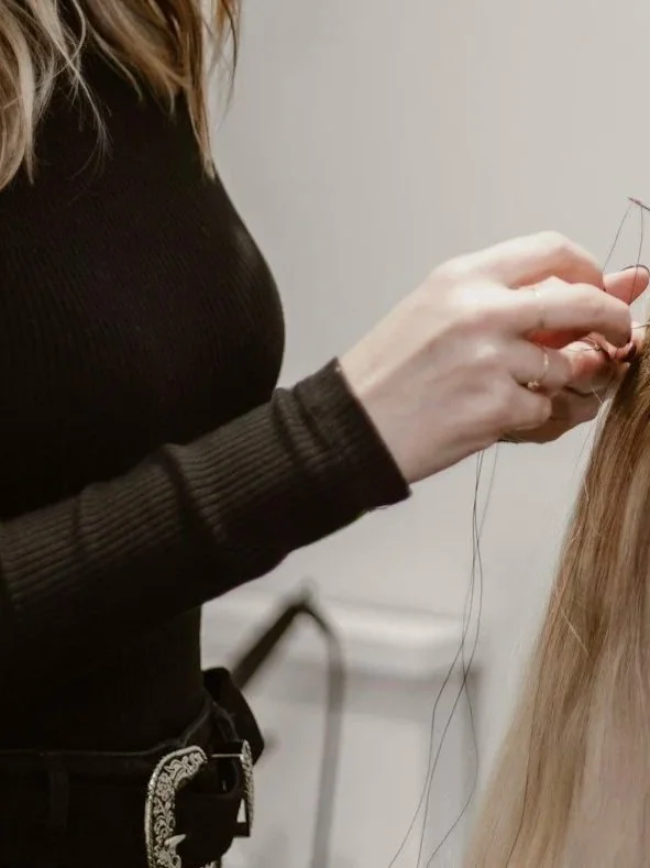 a closeup of a hairstylist's hands, applying the luna method extension method