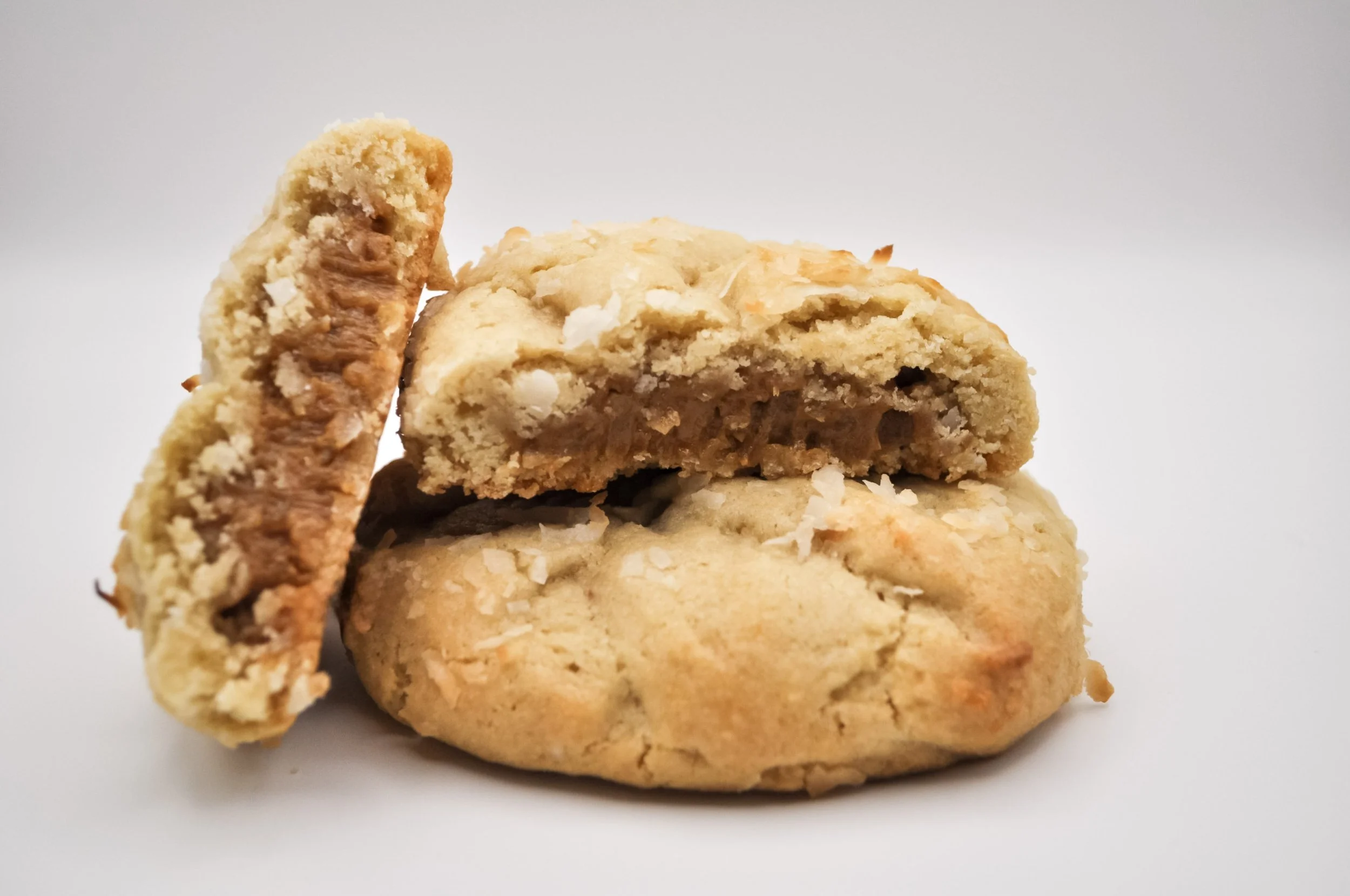 Close-up of two oatmeal cookies stacked with a broken cookie on top, showing the chewy interior, with white chocolate chips and nuts, against a plain white background.