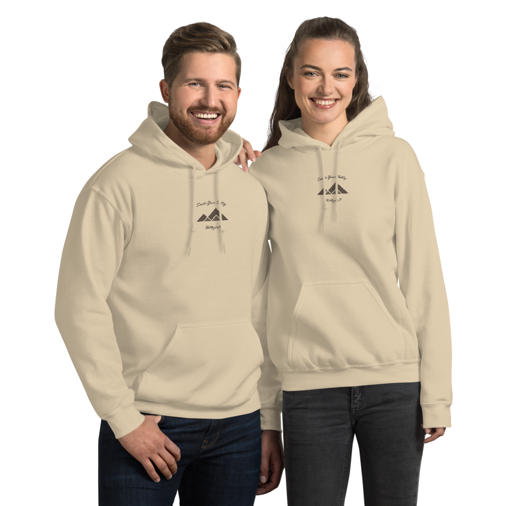 Two smiling young adults, a man and a woman, standing side by side wearing matching cream-colored hoodies with a mountain logo and text, against a black background.