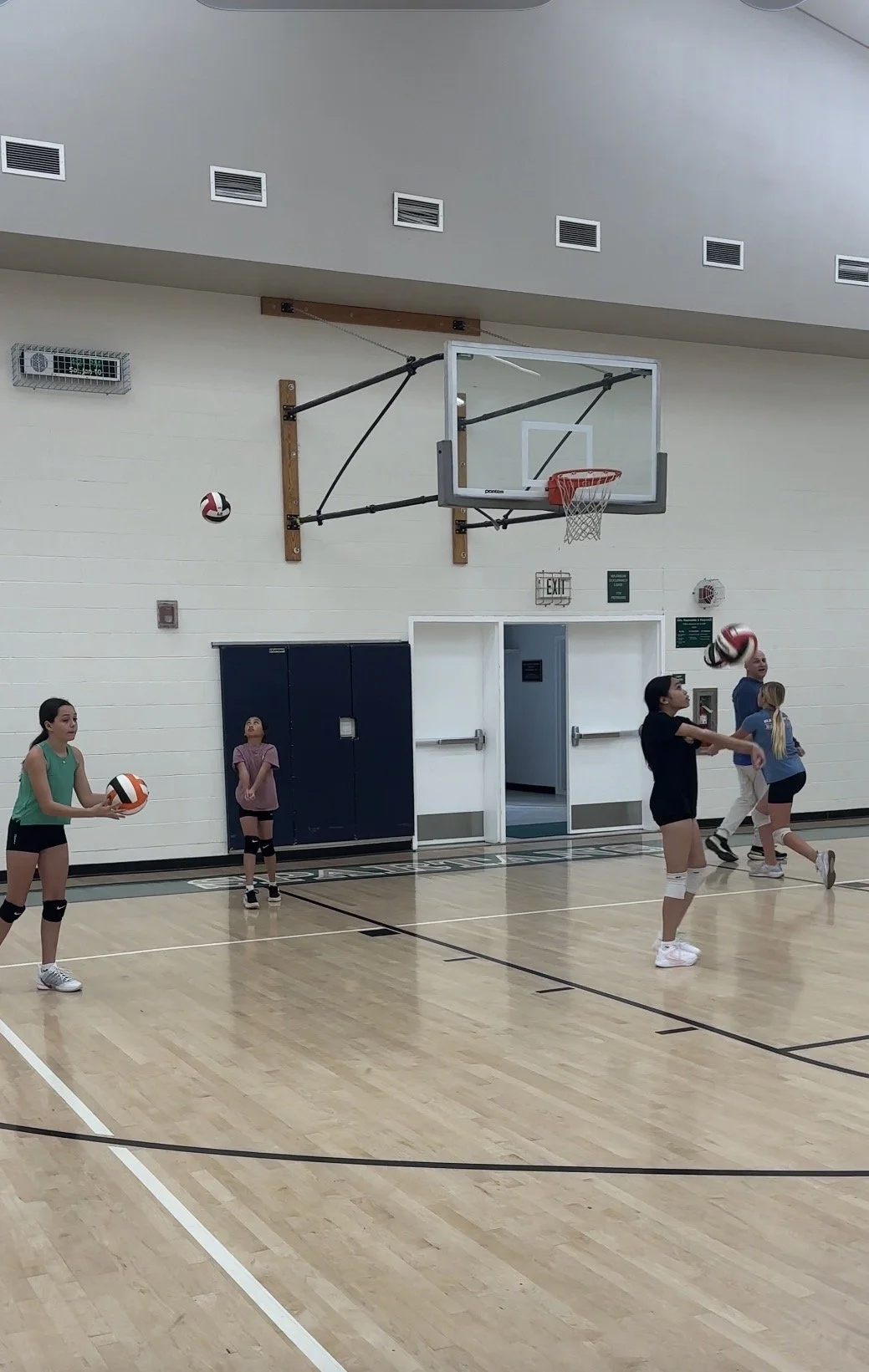 Children practicing volleyball in an indoor gym.