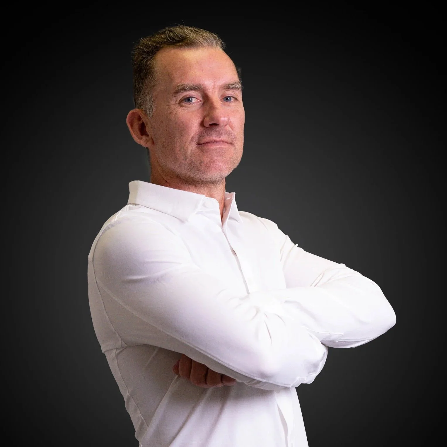 A smiling man with gray hair and beard wearing a navy suit and light blue shirt, standing indoors.