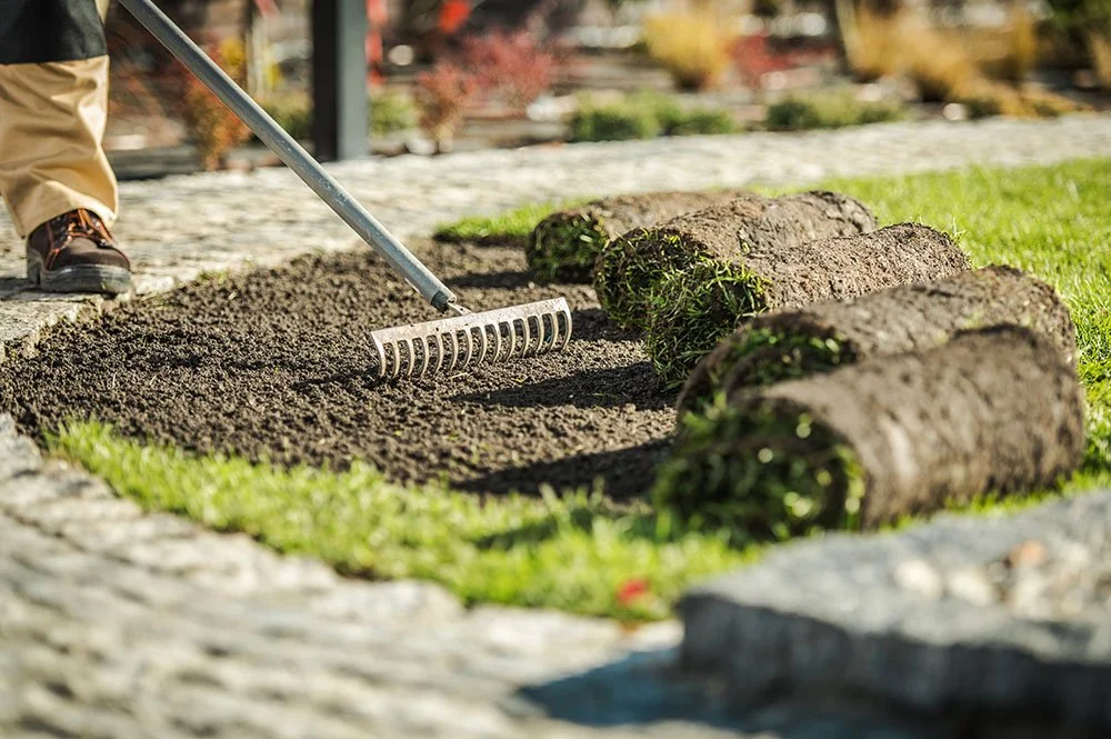 Person laying soil and laying sod to create a garden bed with large logs as border