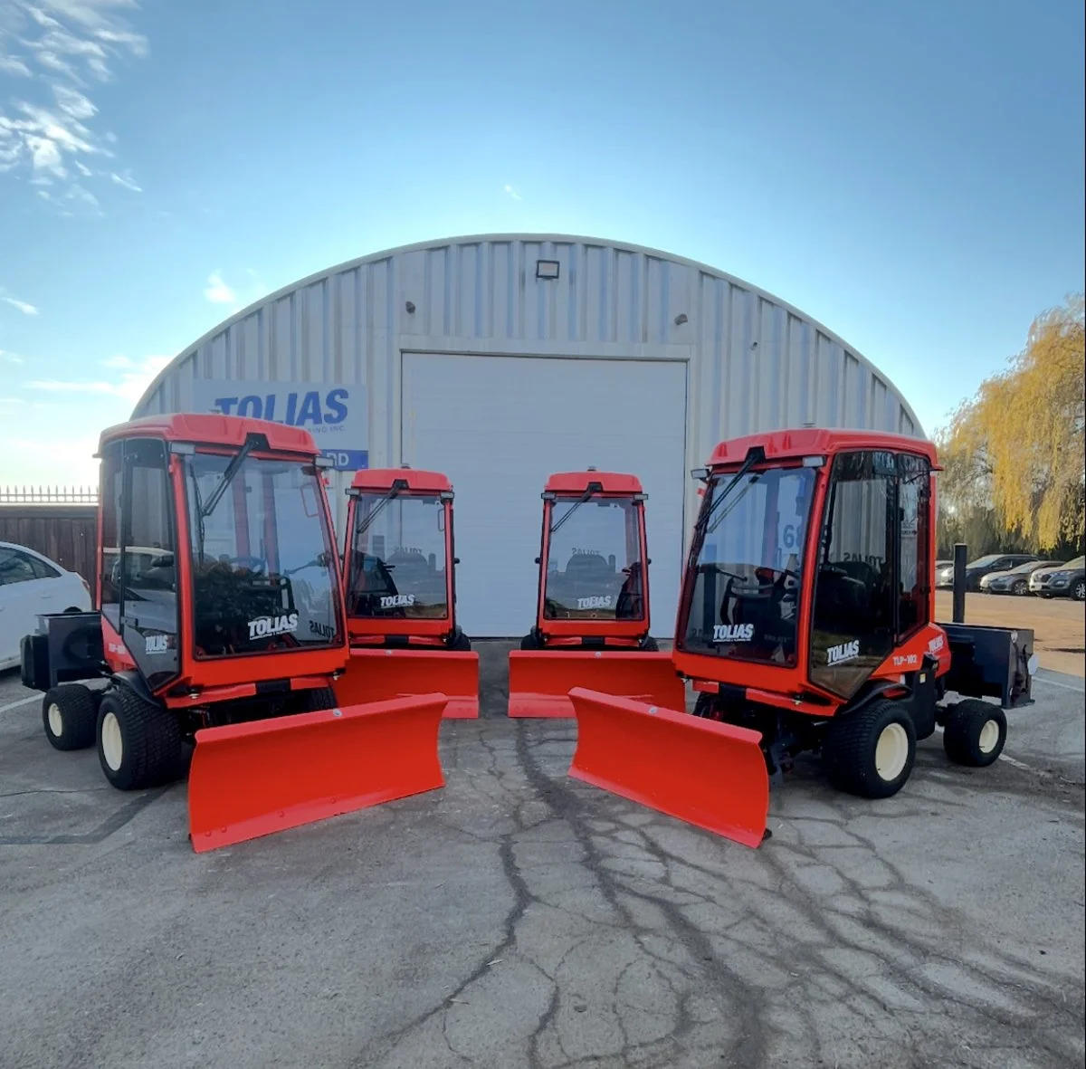 Four red Kubota's parked in front of a salt reserve building with a blue sign that reads 'TOLIAS'.
