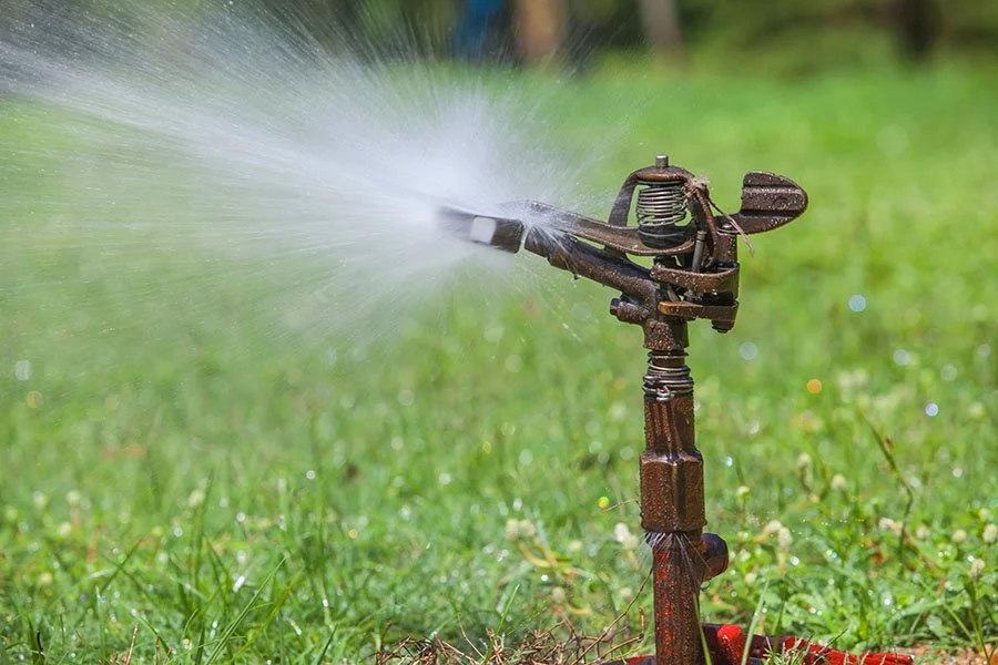 An old rusty garden sprinkler releasing water onto a grassy lawn.