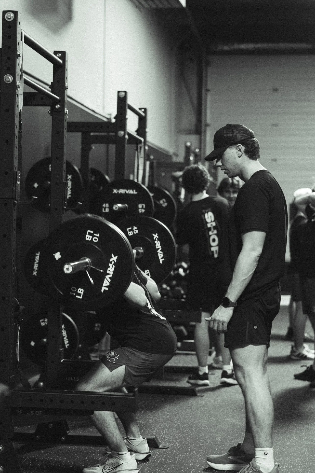 A gym scene with people lifting weights and a coach supervising a person doing squats.