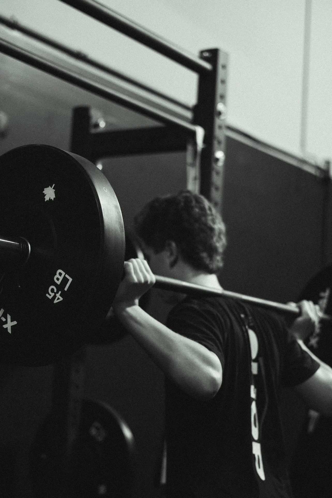Person lifting a barbell in a gym, black and white photo, with weight plates marked 45 LB.
