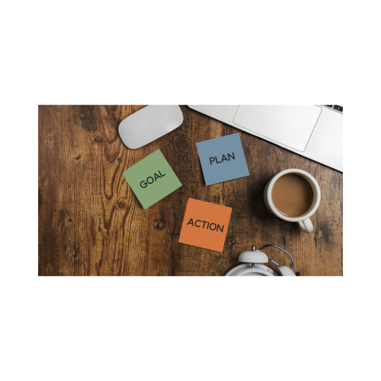 Wooden desk with sticky notes labeled 'GOAL', 'PLAN', and 'ACTION', a laptop, a white computer mouse, a cup of coffee, and a white alarm clock.