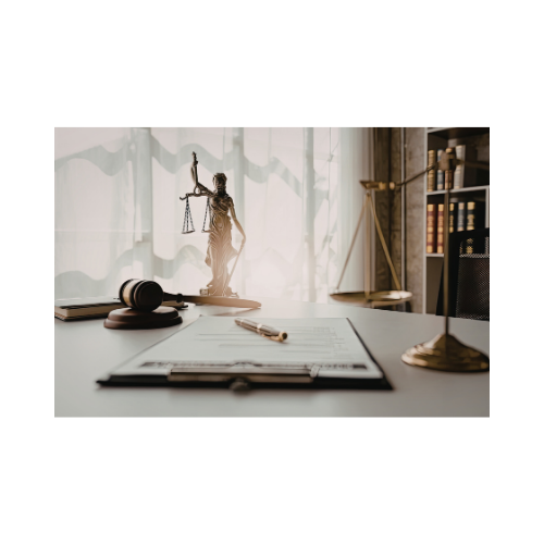 Desk with legal scale, gavel, documents, and statues of Lady Justice in front of a window with sheer curtains.