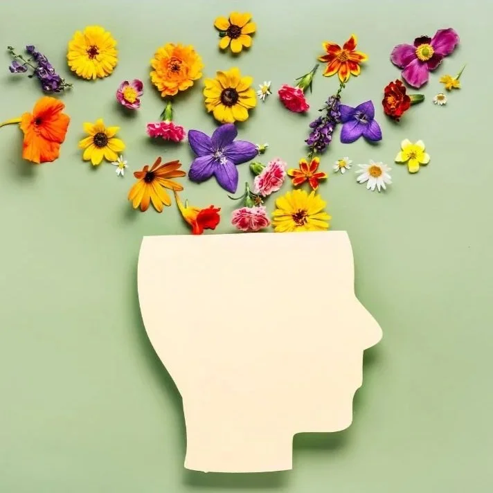 A paper cutout of a human head silhouette on a green background with various colorful flowers arranged as if they are emerging from the head.