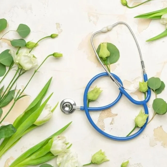 A blue and silver stethoscope surrounded by white and green flowers and green leaves on a light textured surface.
