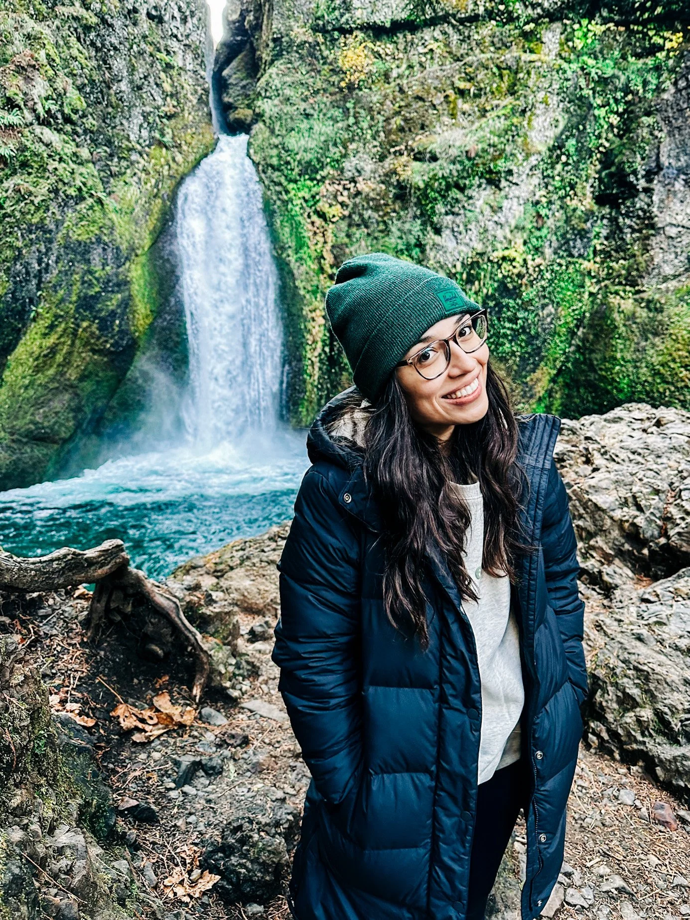 A modern house on a green hill with snow-capped mountains in the background under an overcast sky.