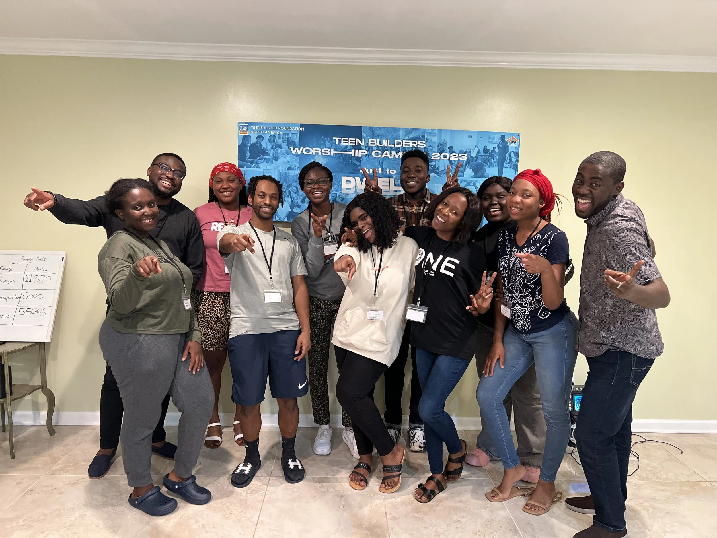 Group of ten diverse young adults smiling and pointing at the camera during a church camp in 2023, standing in front of a blue banner with event details.