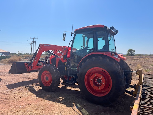 Red tractor with a front loader attachment on a dirt field under a clear blue sky.