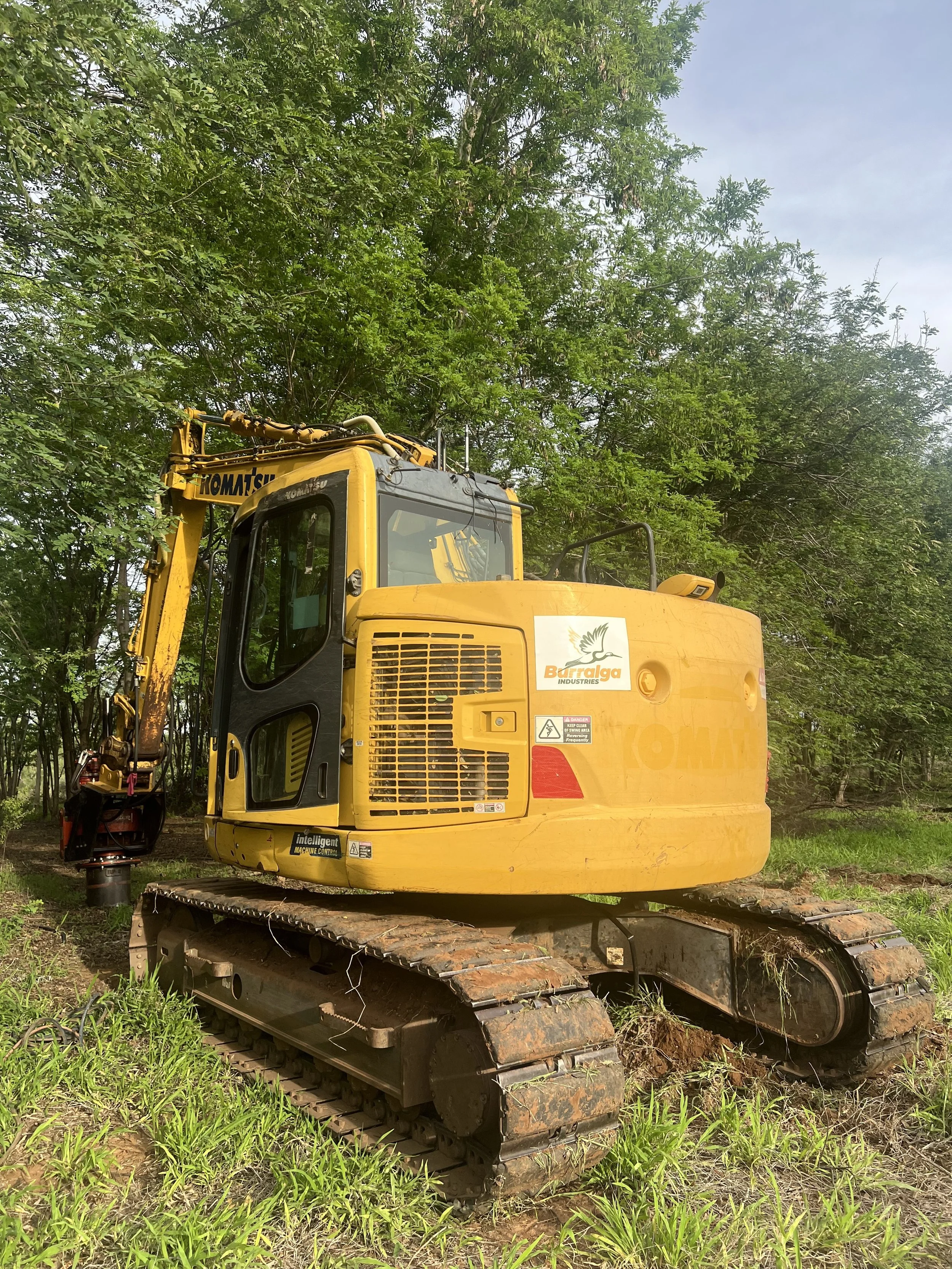 A yellow bulldozer with tracks in a grassy outdoor area, surrounded by green trees and cloudy sky.