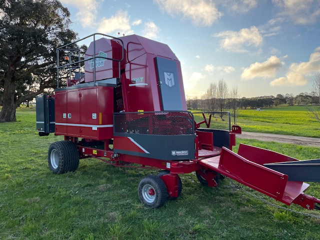 Large red forage harvester machine with black and gray accents on green grass field under partly cloudy sky.