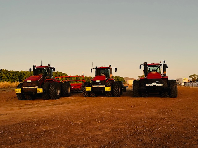 Three large red tractors parked on a dirt field under a clear sky.