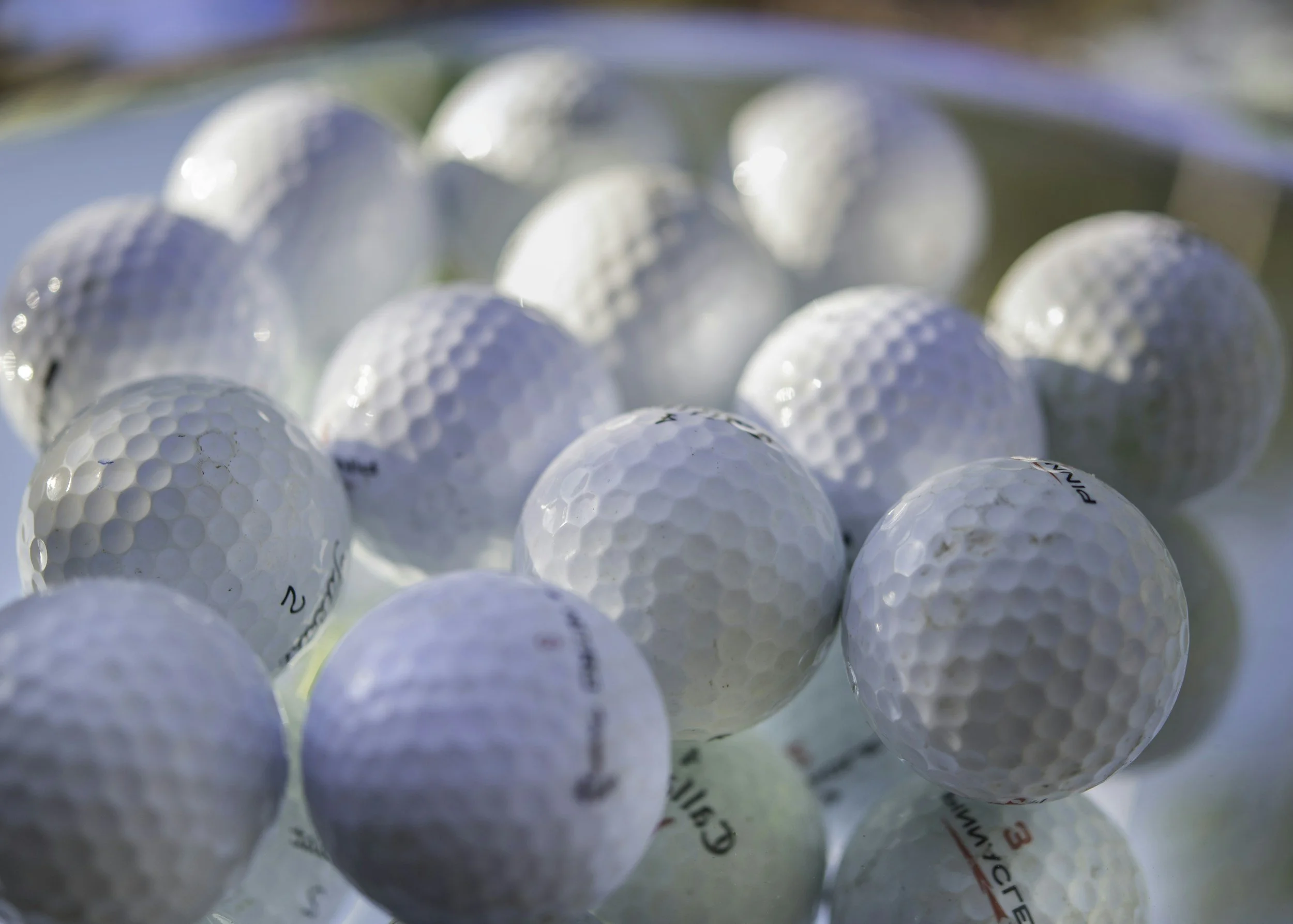 Close-up image of multiple white golf balls scattered together, with some showing brand markings.