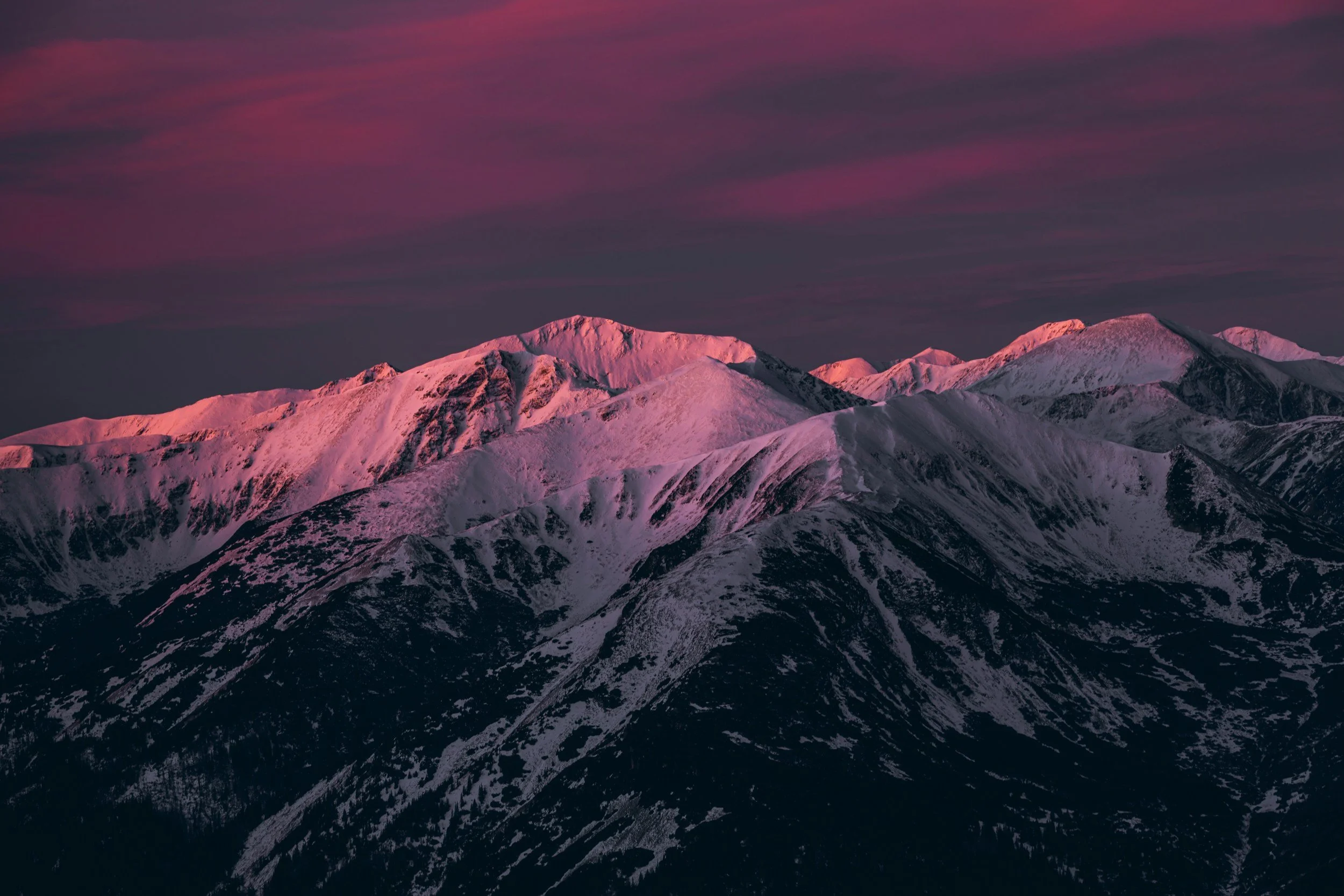 Snow-capped mountain range under pink and purple sky at dusk.