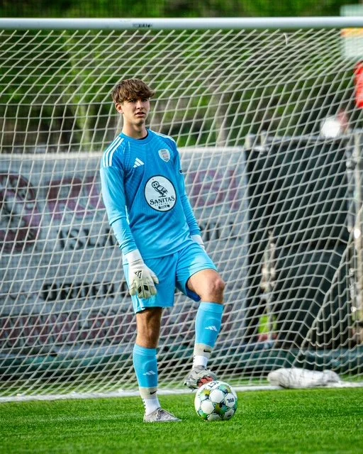 Young male soccer goalkeeper standing with one foot on a soccer ball on the field during a match.