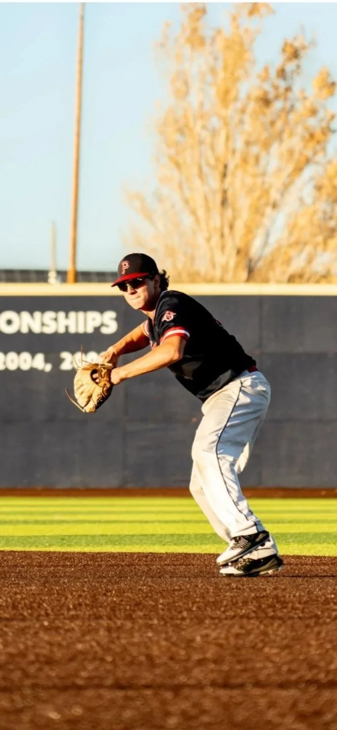 A baseball player in uniform, wearing a black jersey, white pants, and a cap, is fielding a ball on a baseball field during a game.