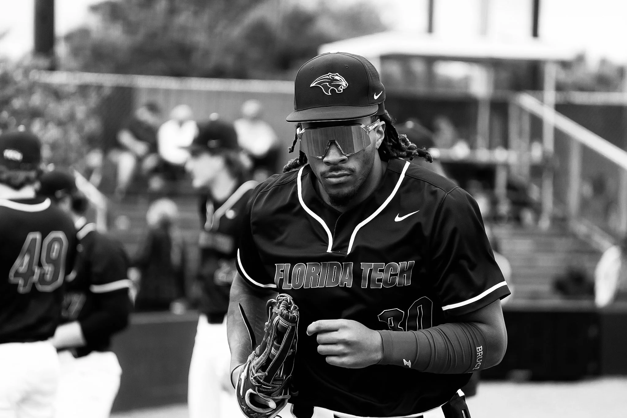 A baseball player wearing a Florida Tech jersey, sports sunglasses, and a Florida Tech cap, holding a baseball glove during a game.