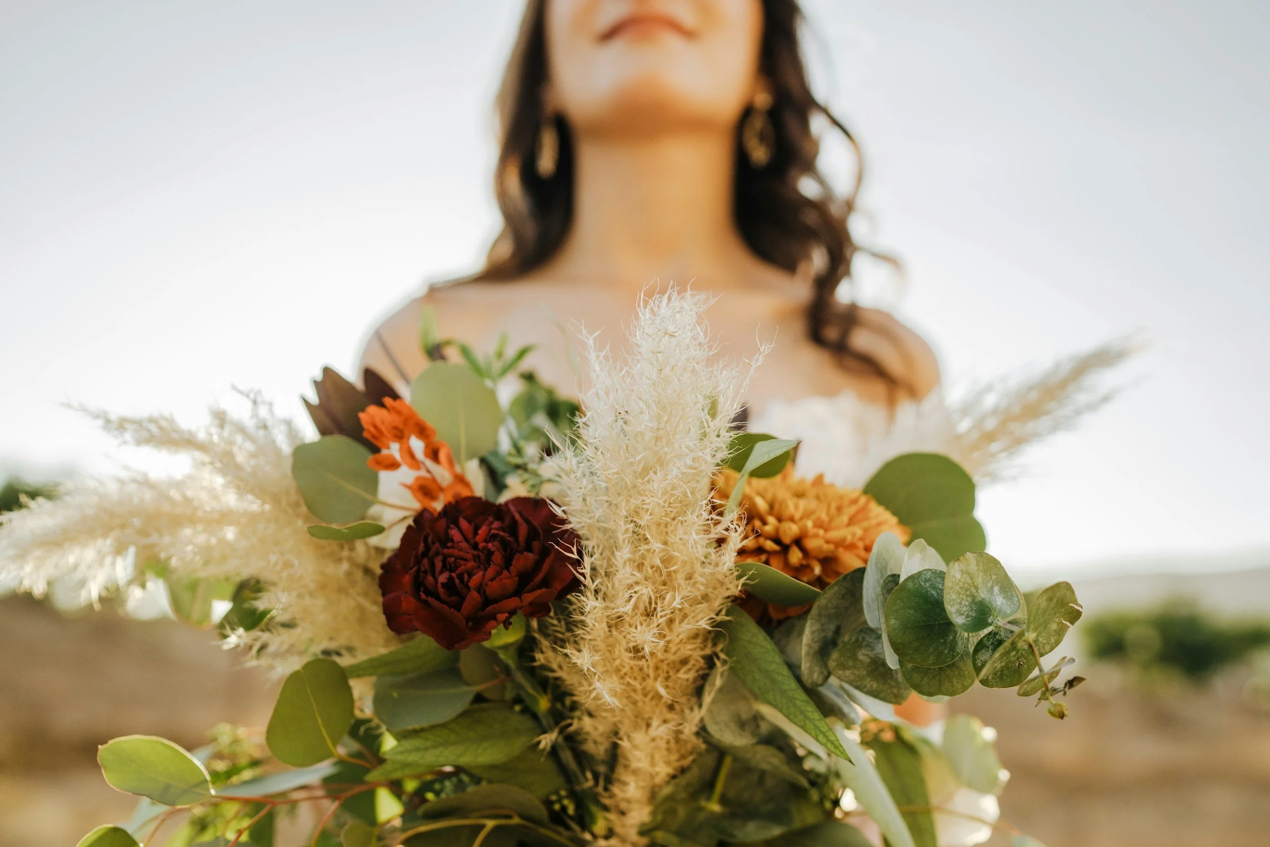 A woman holding a bouquet of flowers, with only her neck and part of her face visible, in front of a bright sky.