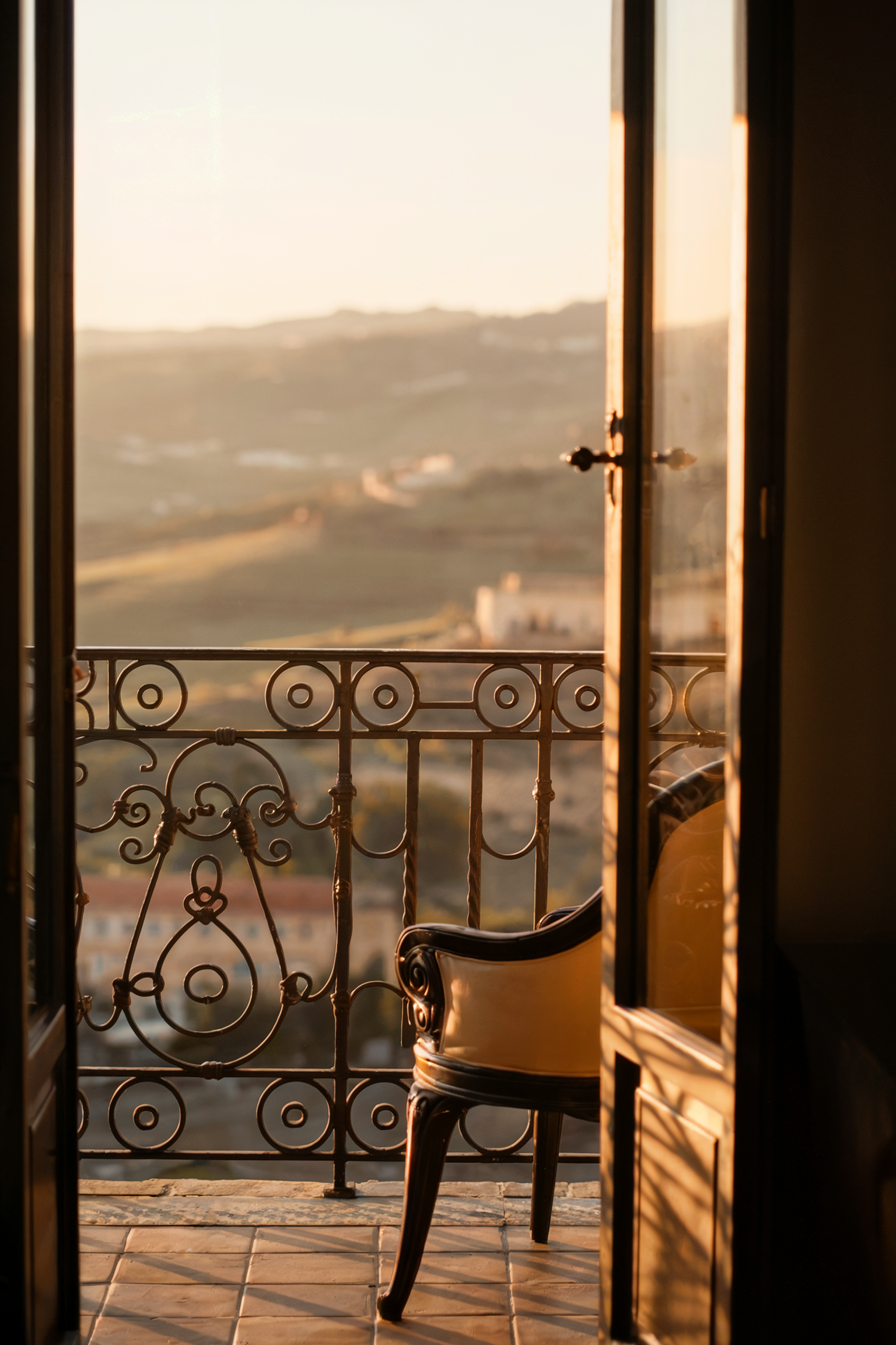 French balcony with wrought iron railing and elegant chair overlooking golden sunset cityscape for romantic travel
