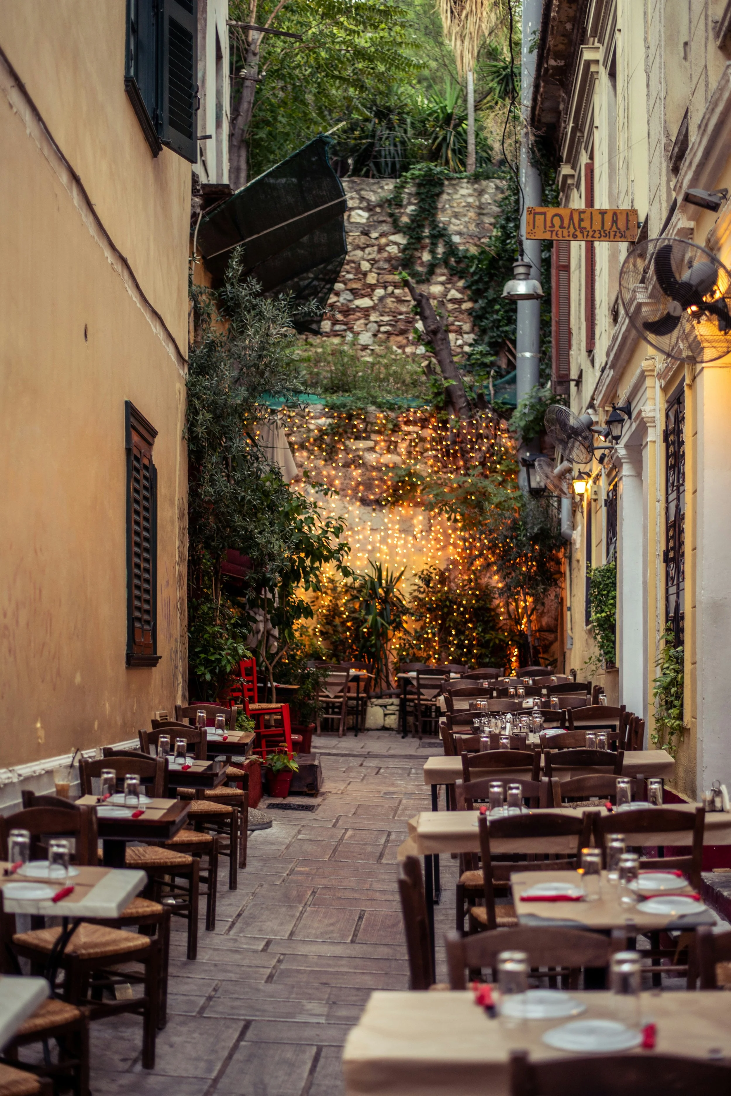 Intimate Italian courtyard restaurant with ivy-covered stone walls, wooden tables, and warm string lights at dusk