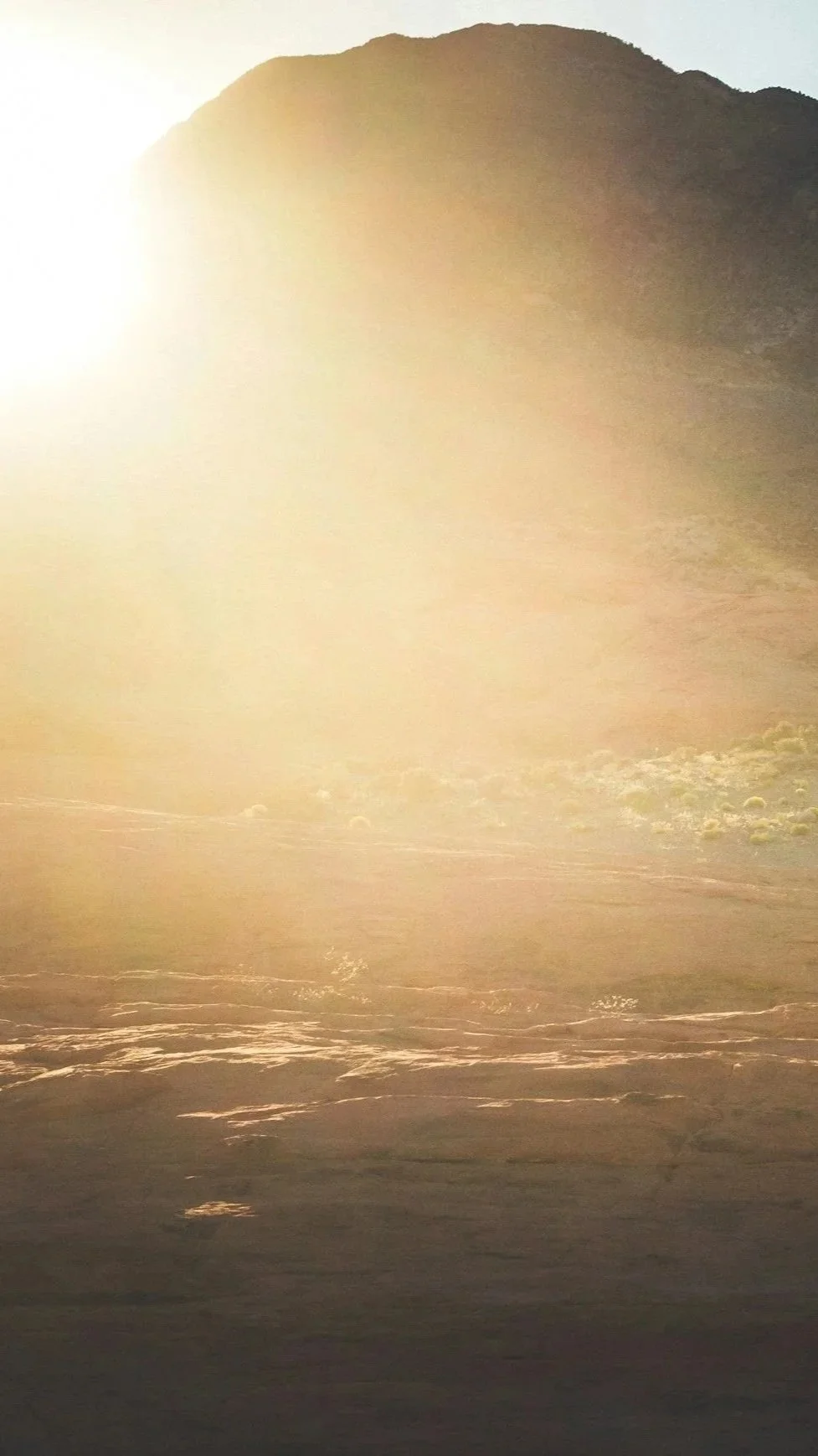 A mountainous landscape during sunset or sunrise with sunlight illuminating the scene.