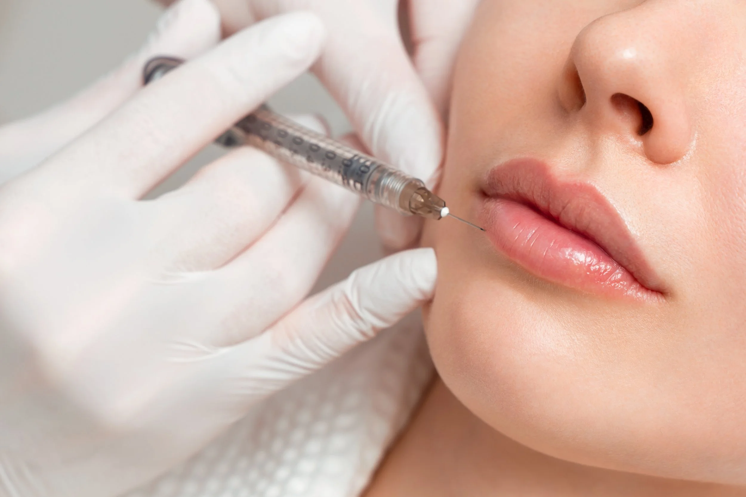 A person receiving a cosmetic injection in the lips from a healthcare professional wearing gloves.