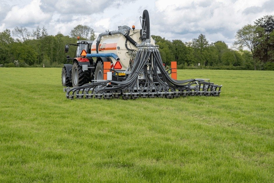 A tractor with a large tank and connected spraying equipment is in a green field, likely spraying fertilizer or pesticides.