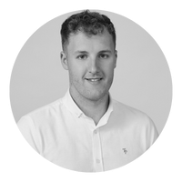 Black and white portrait of a young man with short curly hair, wearing a collared shirt, smiling softly.