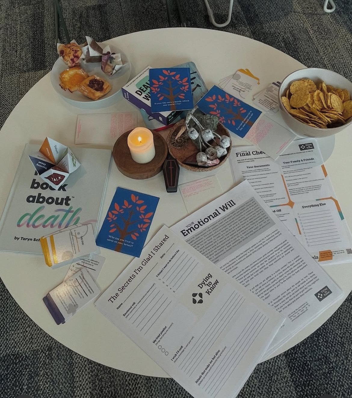 A table with books, papers, candles, medication, snacks, and informational materials, set up for a Death Cafe. death.