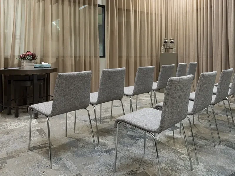 A room with grey cloth chairs lined up in front of a window that is mostly covered by a linen curtain. A cremation witnessing room at Springvale Botanical Cemetery