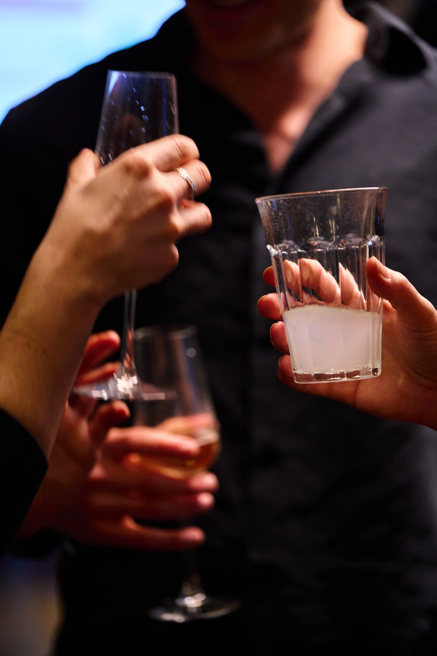 People holding glasses of water in a toast, seen in a close-up at a social gathering.