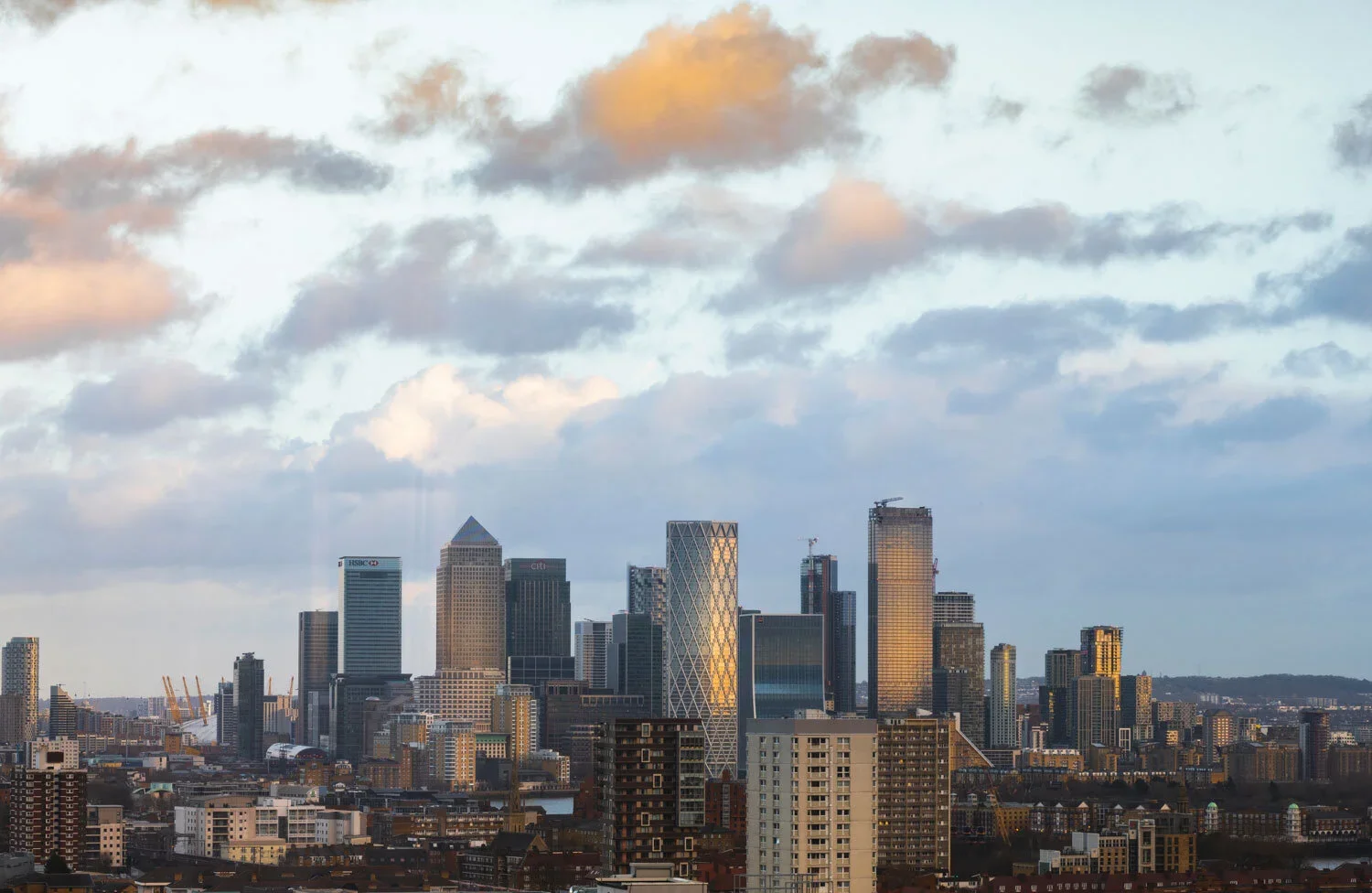 A city skyline with tall modern skyscrapers under a partly cloudy sky during sunset.