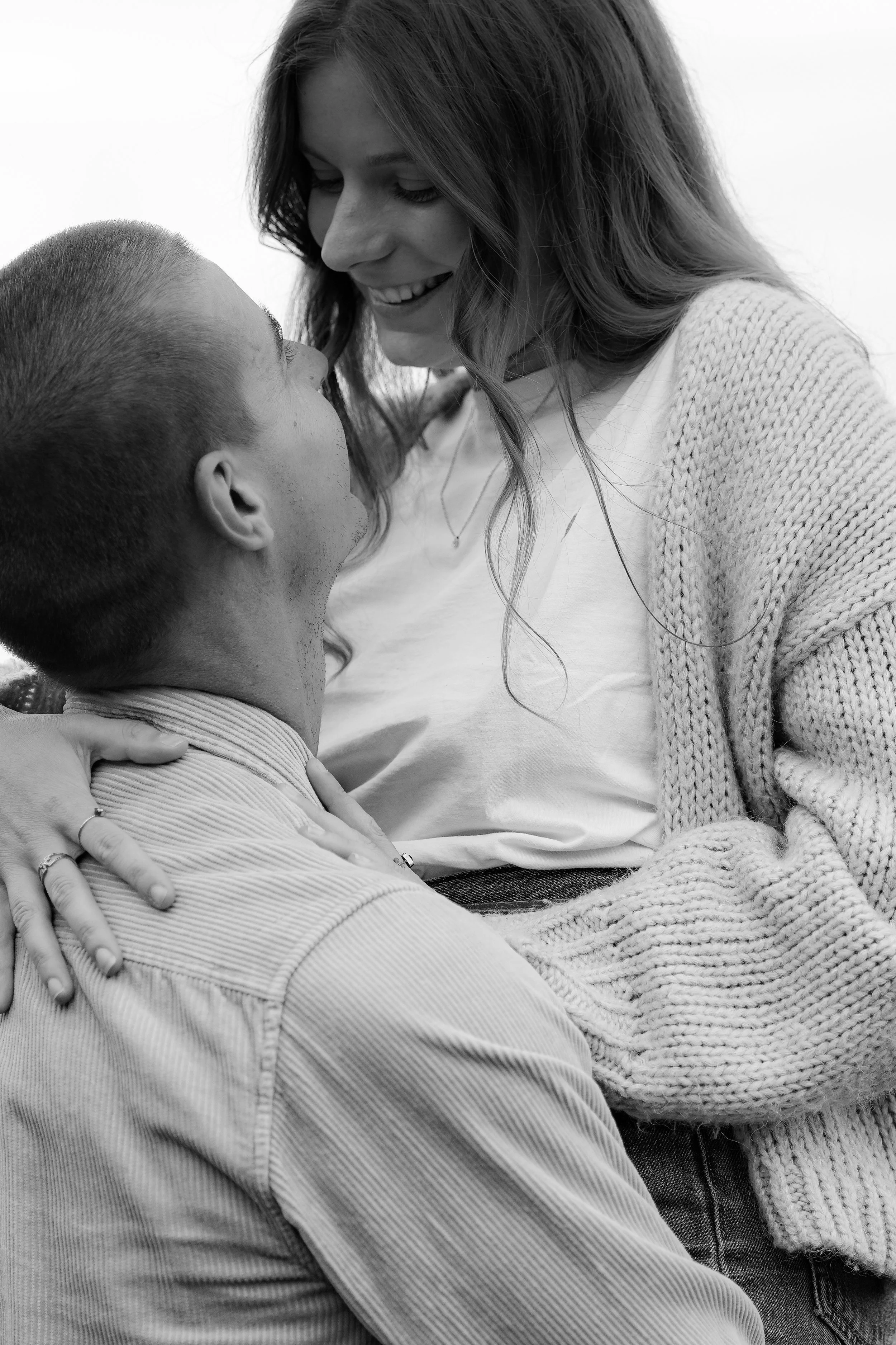 Une femme et un homme en train de partager un moment affectueux, avec la femme souriante et l'homme regardant vers elle, en noir et blanc.