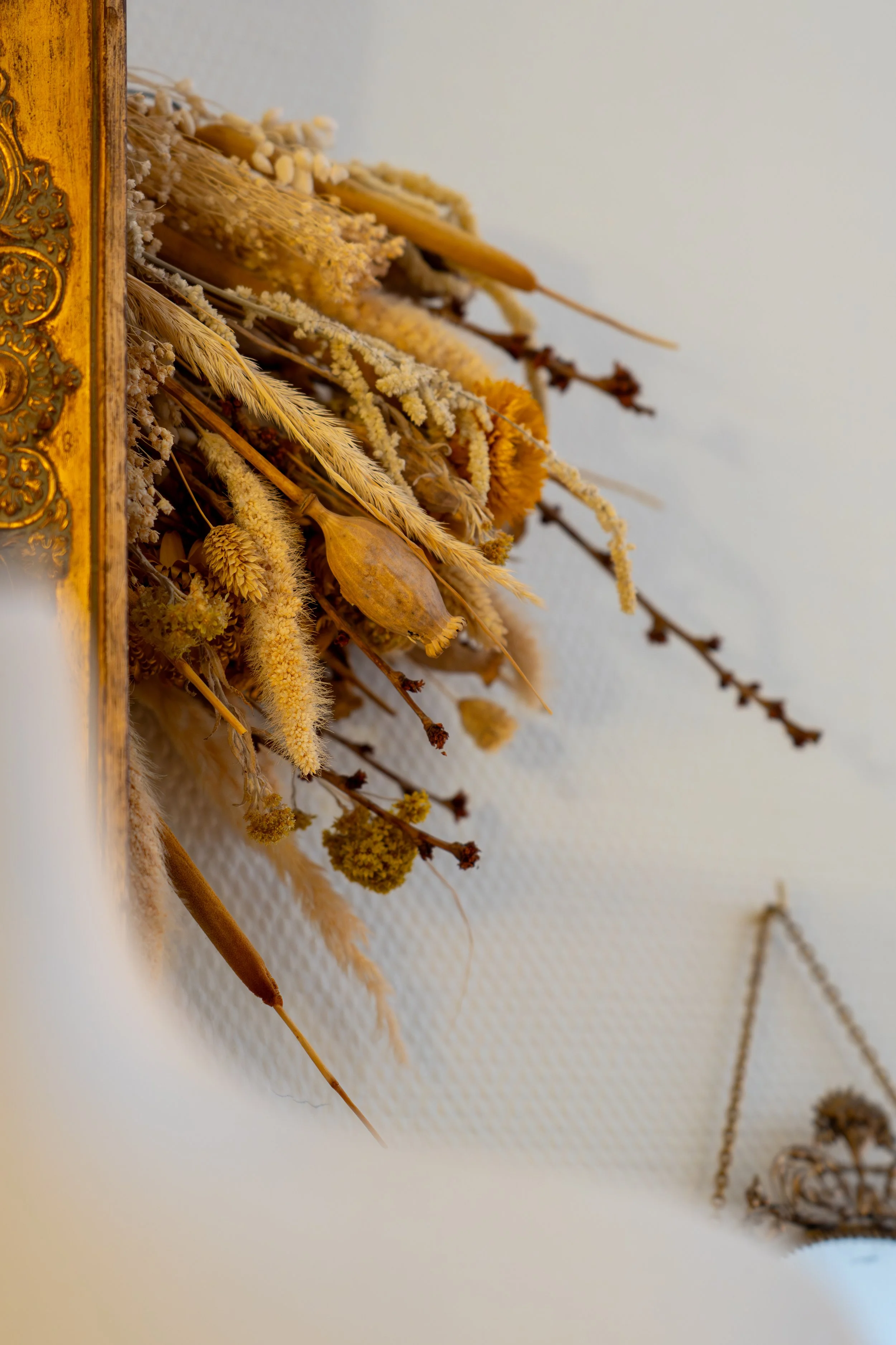 Un bouquet de fleurs séchées suspendu au mur à côté d'un ornement doré et d'une balance.