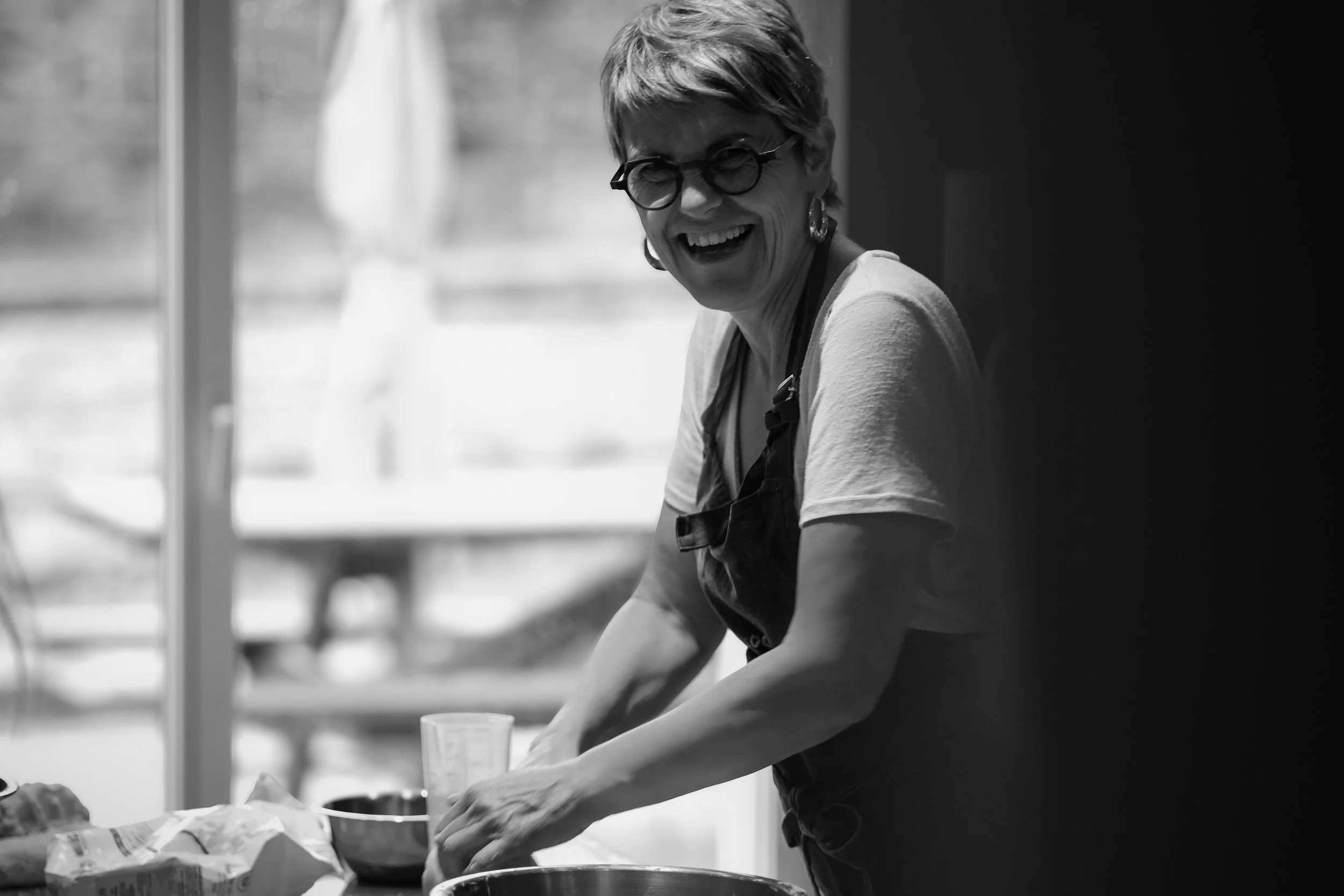 Une femme souriante en train de cuisiner dans une cuisine, vue en noir et blanc.