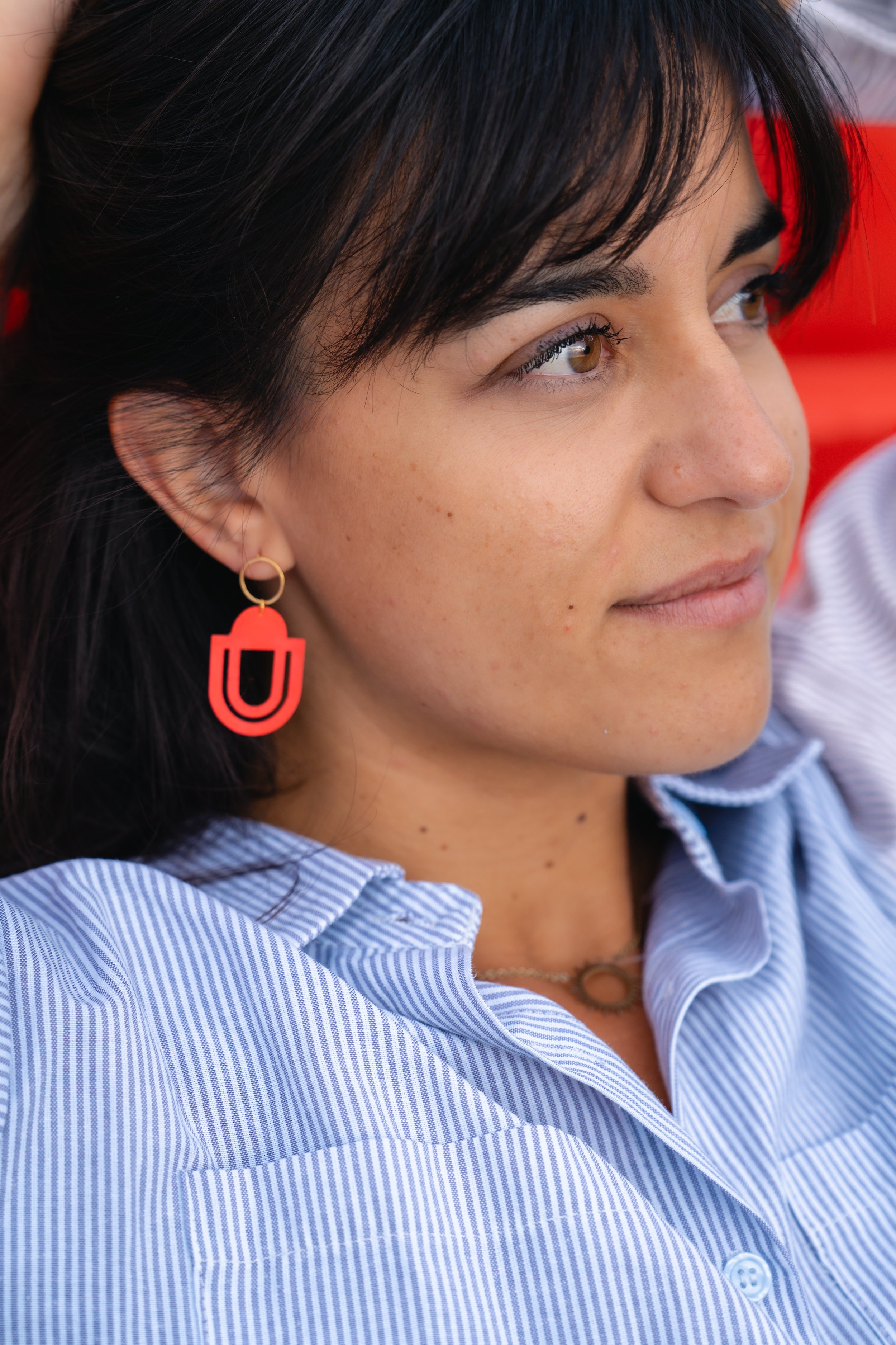 Jeune femme avec boucle d'oreille rouge et chemise à rayures bleues, regardant à droite.
