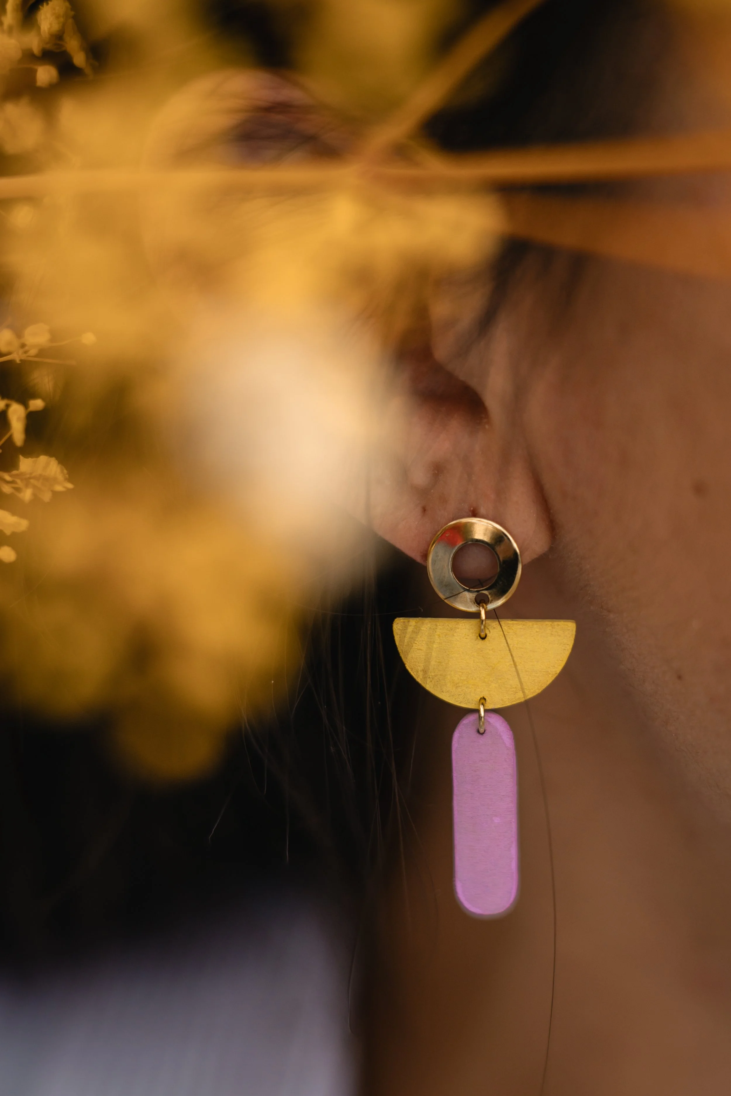 Une personne porte une boucle d'oreille colorée et une casquette, avec des fleurs floues au premier plan.